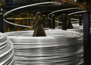 工場で製造中の巨大な銀色のワイヤーコイル。銀色に光るワイヤーが機械に巻き取られている。