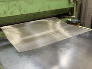 平織金網をの在庫をレベラーで伸ばして加工準備をしている作業風景