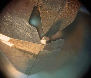 研磨され、光を反射するパンチングメタル用ドリルの刃先を拡大鏡で確認している様子。