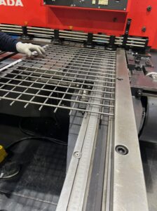 溶接金網の製造工程。作業員が機械にセットされた金網の寸法を、定規(スケール)を使って確認している様子。