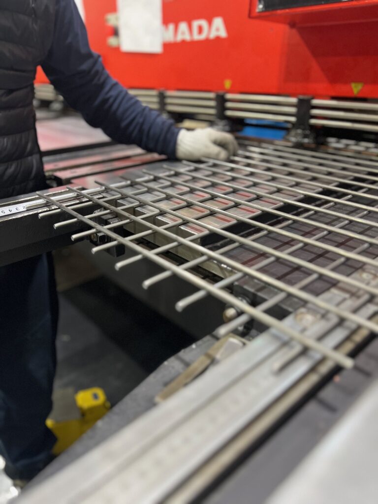 溶接金網を扱う作業員のクローズアップ。作業員は手袋を着用し、機械で金網の寸法を調整している様子。