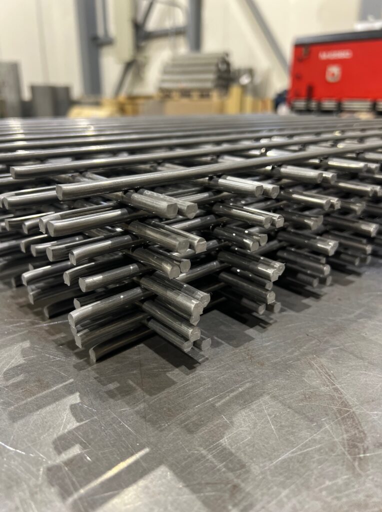 製造工場で平積みされた、多数の溶接金網の束。金属の光沢があり、規則的なメッシュ構造がはっきりと見える。