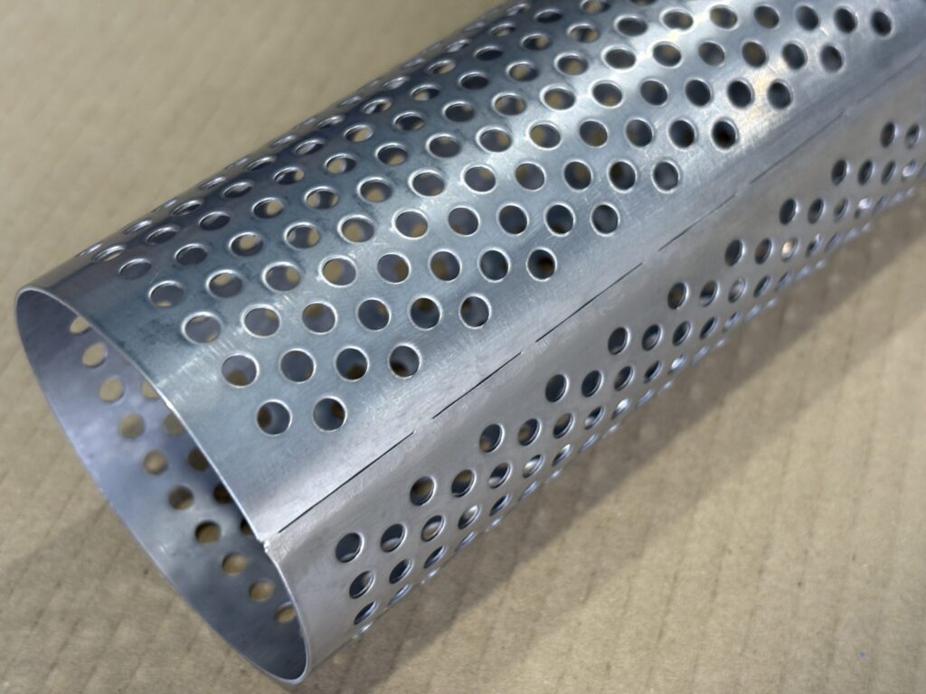 ステンレス製の有孔パイプ（パンチングメタルをロール加工したもの）の接合部をクローズアップ。板の突き合わせラインが明確に見え、そのライン上には穴がない余白が設けられている。